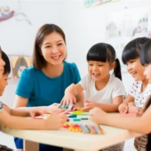 A-happy-adult-caregiver-interacting-with-elementary-school-children-in-a-bright-classroom.