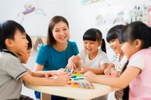 A-happy-adult-caregiver-interacting-with-elementary-school-children-in-a-bright-classroom.
