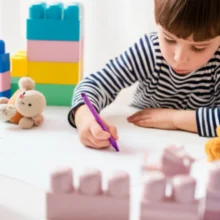 A-child-drawing-on-the-floor-surrounded-by-toys,-symbolizing-creativity-and-a-nurturing-environment.